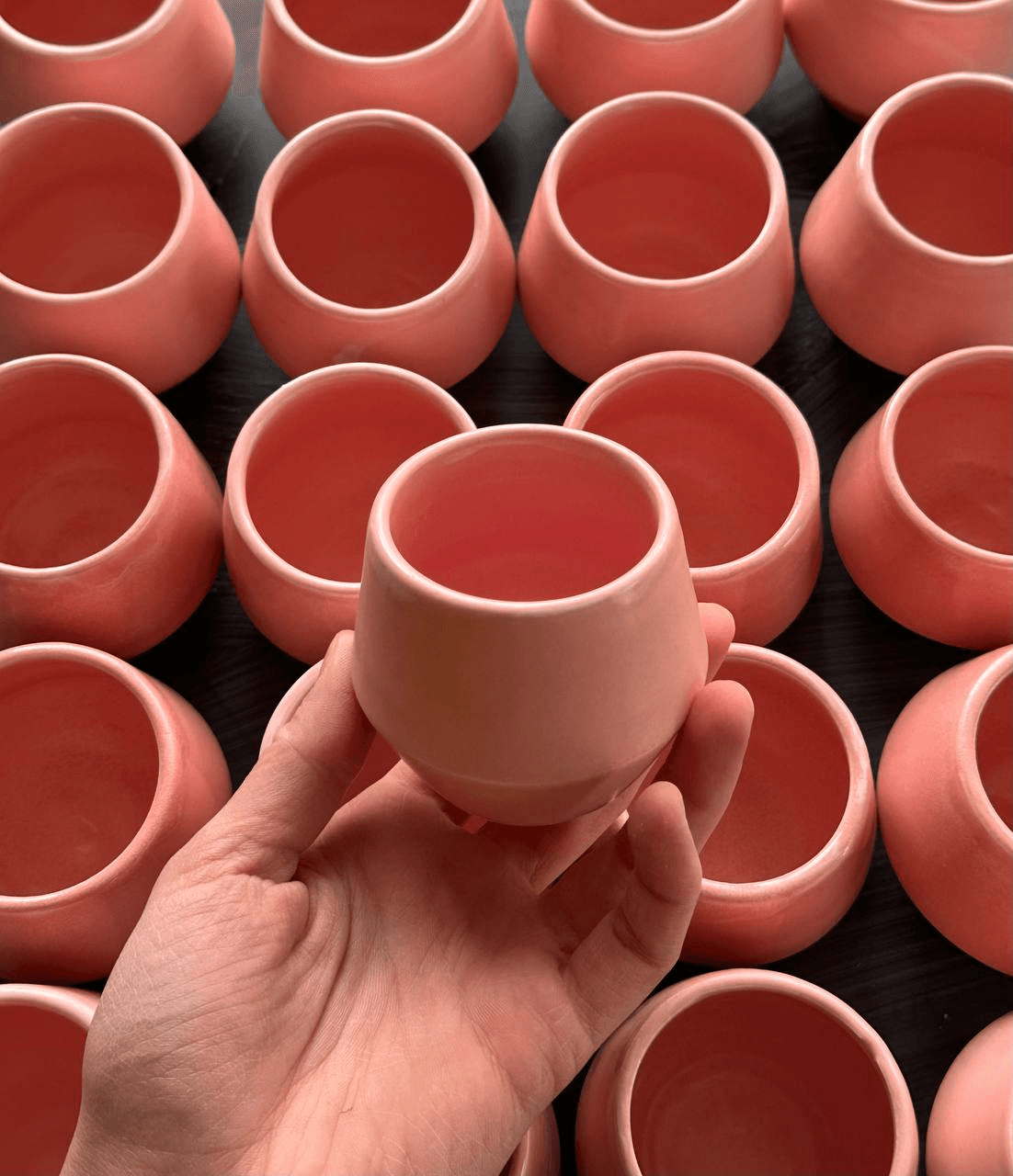 Różowa ceramiczna czarka trzymana w dłoni na tle innych różowych czarek z kolekcji